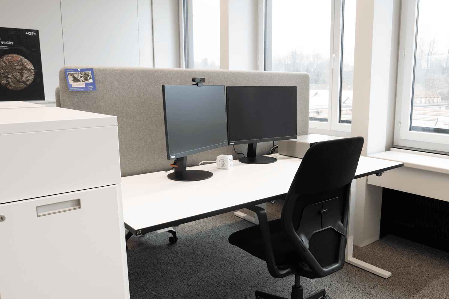 Seitenansicht auf einen Arbeitsplatz mit Akustikwand, B&uuml;rodrehstuhl und separaten Bildschirmen